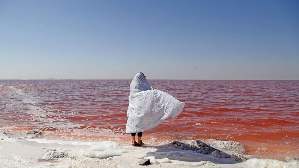 Человек в белом платке стоит на берегу озера Урмия и его вода красного цвета