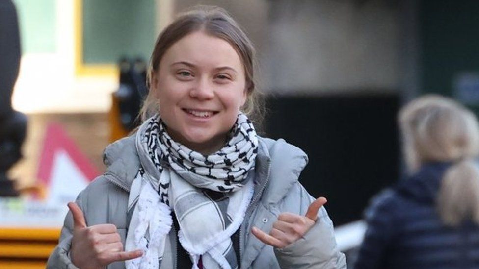 Greta Thunberg smiling and making 'rock on' hand signs as she made her way past photographers