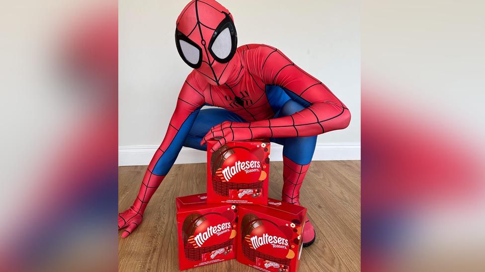 Spiderman wearing his suit crouched in front of Easter Egg boxes