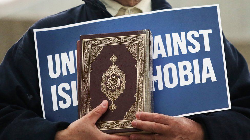 Person carrying 'unite against Islamophobia' sign and a Koran