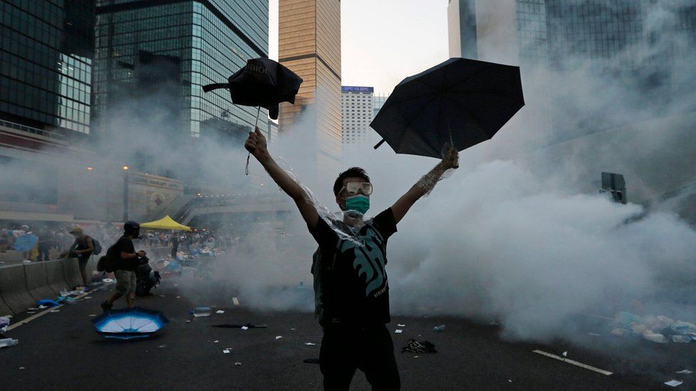 A protester (C) raises his umbrellas in front of tear gas which was fired by riot police to disperse protesters blocking the main street to the financial Central district outside the government headquarters in Hong Kong, September 28, 2014.
