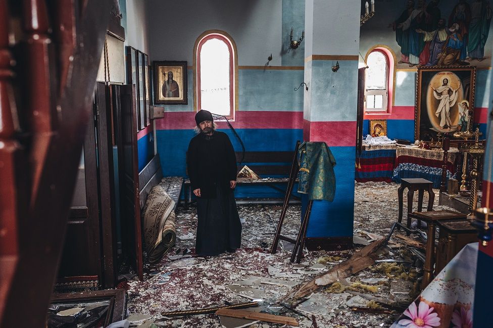 Priest Romanov is seen inside a damaged church following recent shellings in Yasnohorodka,