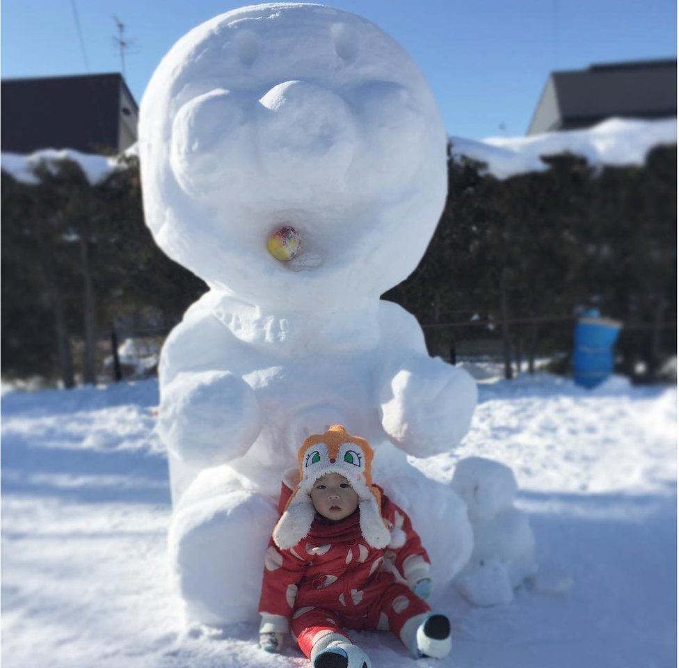 An Anpanman character made of snow, with a baby sitting below it.