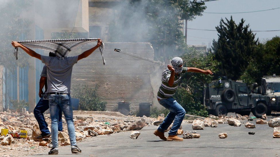 A Palestinian protester uses a slingshot to hurl stones towards Israeli security forces during clashes following a weekly demonstration against the expropriation of Palestinian land by Israel on 1 July