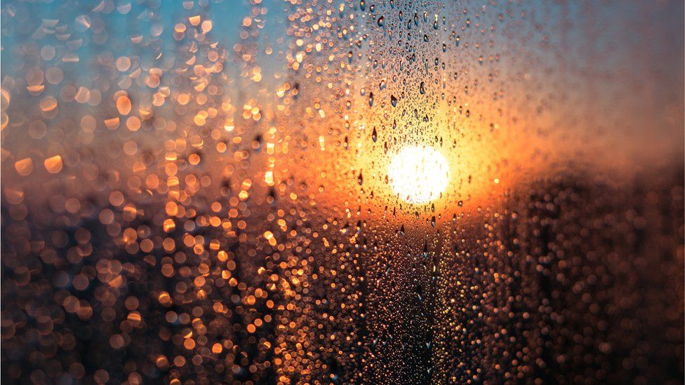 Мокрое окно с конденсированной водой на фоне восхода или заката в холодный зимний день