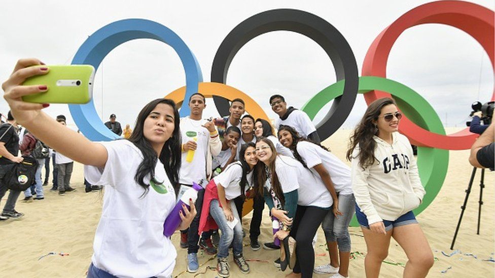 People taking selfies with Olympic rings on a beach in Rio