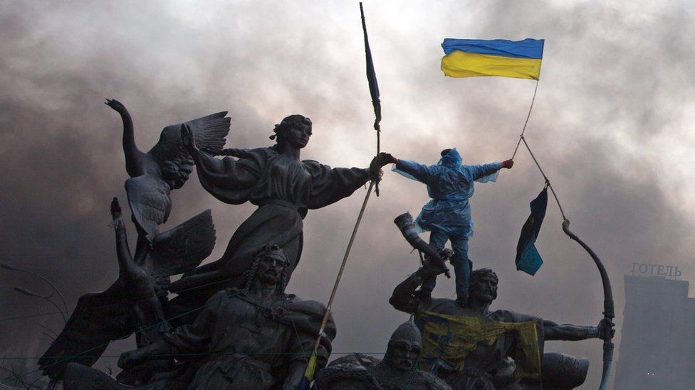 Anti-government protester waves the national flag from the top of a statue during clashes with riot police in the Independence Square in Kiev February 20, 2014