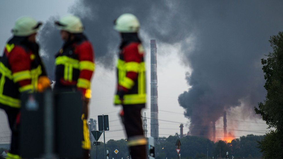 Firefighters stand next to the site of a refinery of Bayernoil company where the explosion took place
