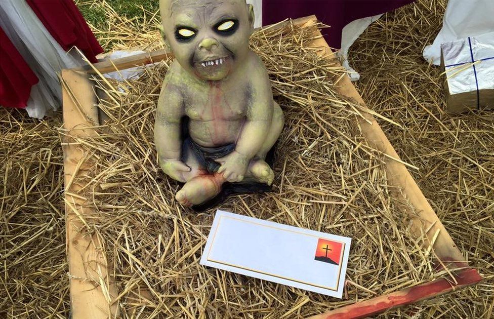 An envelope sits in front of a sculpture of a demon child
