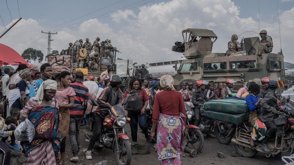 People gather next to some vehicles from the South African National Defence Force (SANDF) as part of the Southern African Development Community (Sadc) Mission as they flee the Masisi territory following clashes between M23 rebels and government forces, at a road near Sake - 7 February 2024