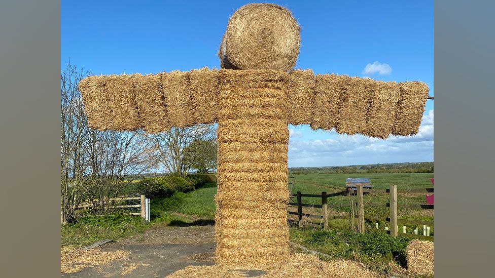 Straw bale structure inspired by the Angel of the North with a round bale head and long wings out on either side