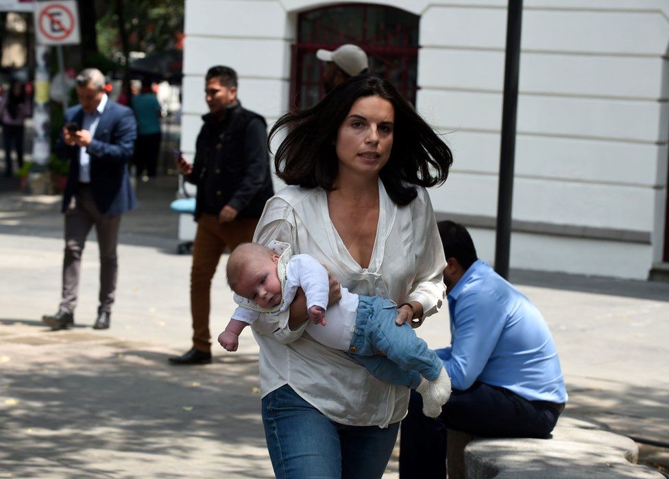 A woman rushes with her baby through the streets after a quake rattled Mexico City on 19 September
