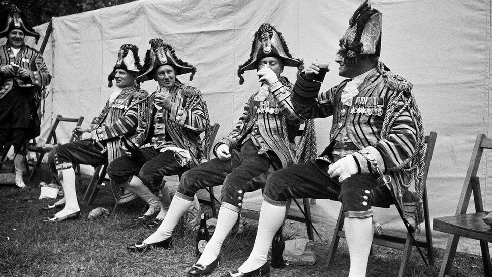 Royal footmen, dressed in glittering uniforms instead of their usual blue battledress raise the glasses in a toast to the Queen 1953
