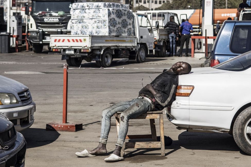 A car wash attendant asleep on a chair with his head resting on a vehicle, Lusaka, Zambia - Tuesday 10 August 2021