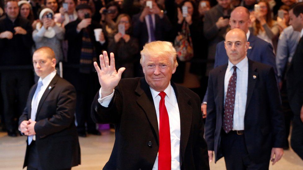 Donald Trump waves to the crowd as he leaves the New York Times building following a meeting, 22 November
