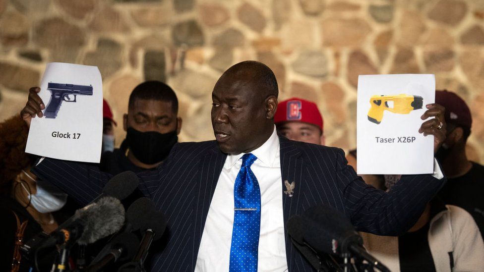 Attorney Ben Crump holds up pictures of gun and a taser during a press conference with the family of Daunte Wright