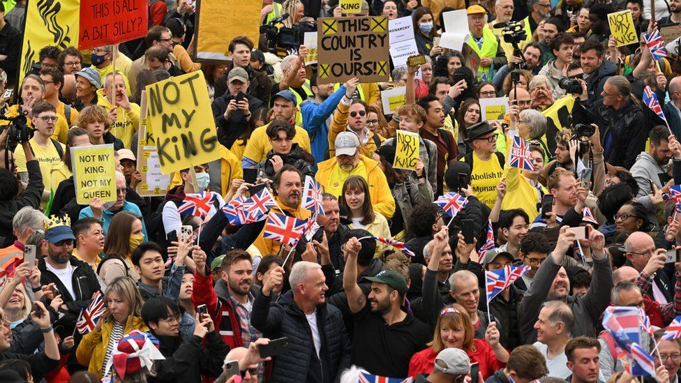 Anti-monarchy protesters standing behind people carrying Union flags to watch the Coronation