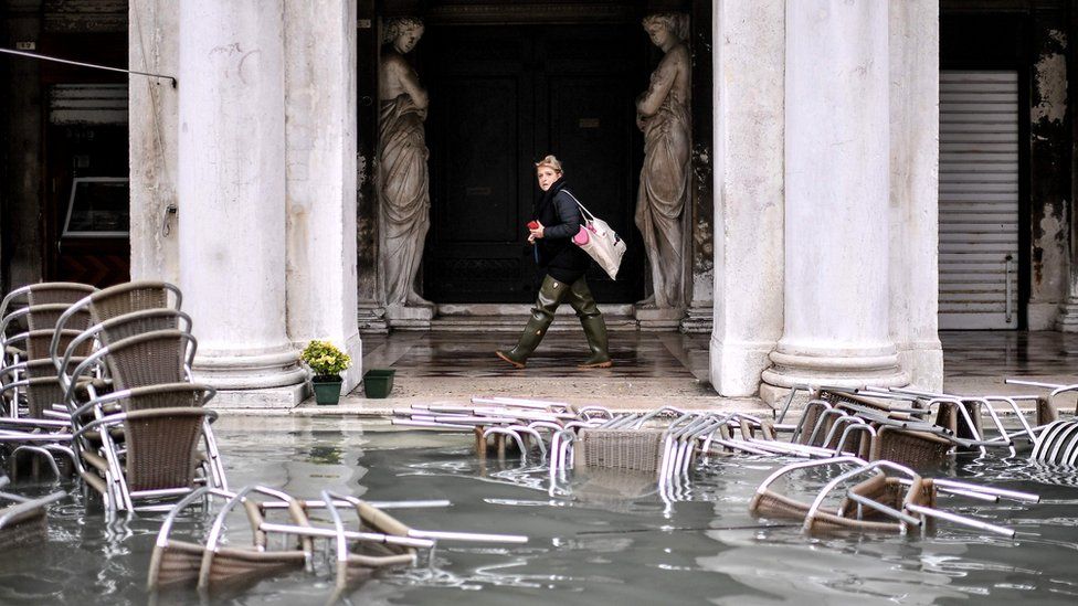 A woman walks past flooded furniture of a cafe terrace as Venice suffers in extremely high water levels, 13 November 2019