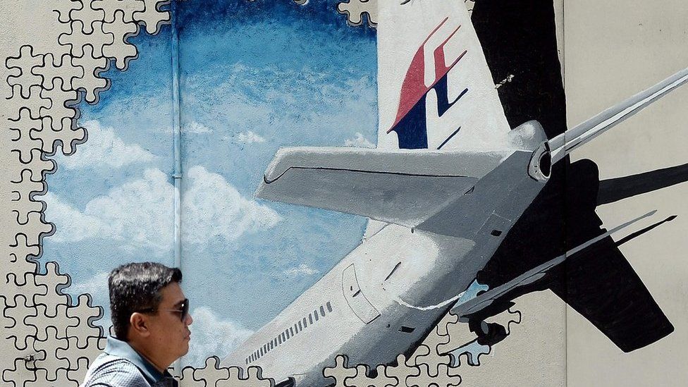 Picture taken on 8 March 2016 shows a man walking in front of a mural of missing MH370 in a back-alley in Kuala Lumpur.