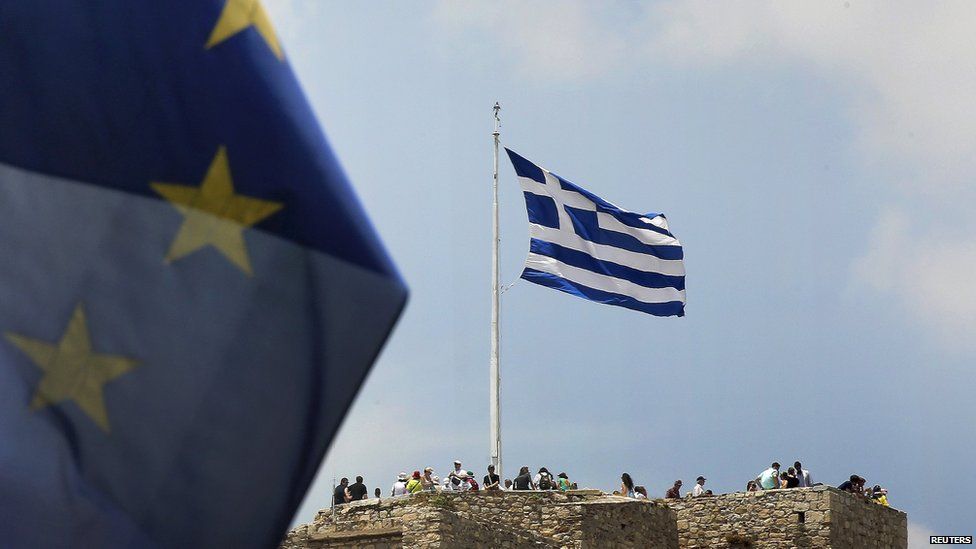 A European Union flag flutters as tourists gather around a Greek flag atop the Acropolis hill in Athens