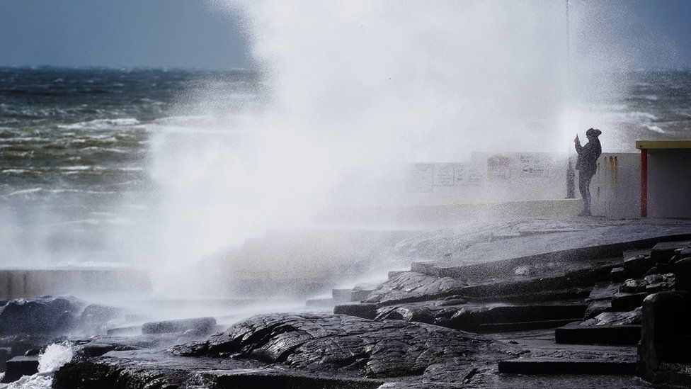 A man takes a photo of the waves at Salthill in County Galway