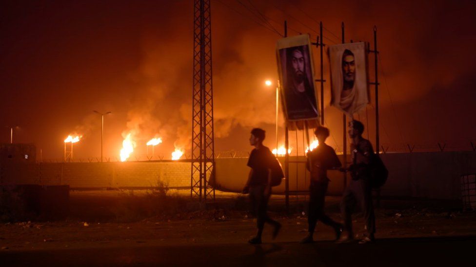 Three young men walk past flares in the Gulf