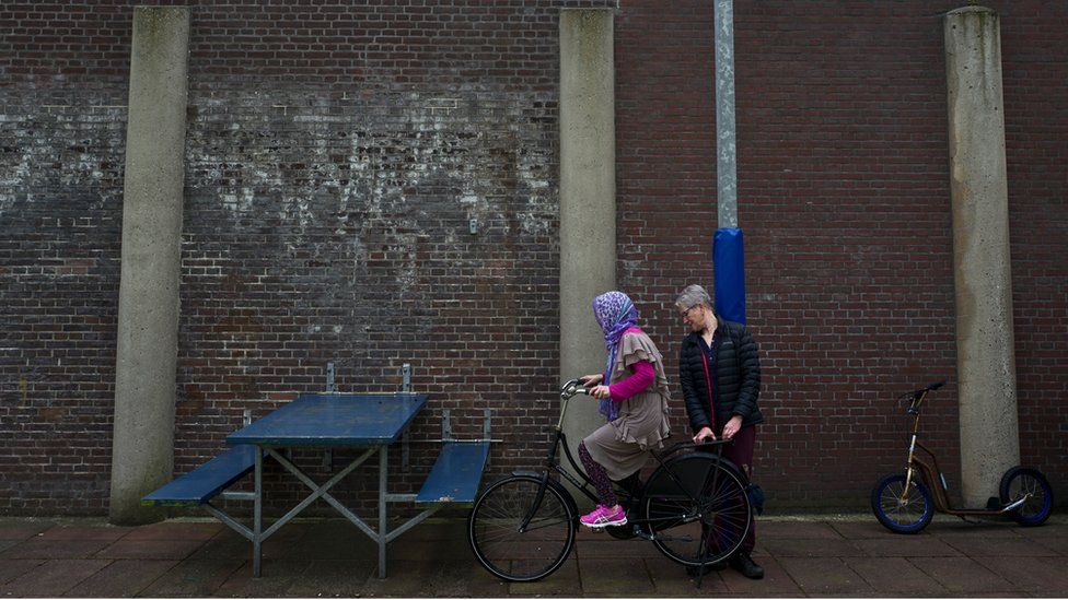 A Dutch volunteer teaches an Afghan refugee woman how to ride a bicycle