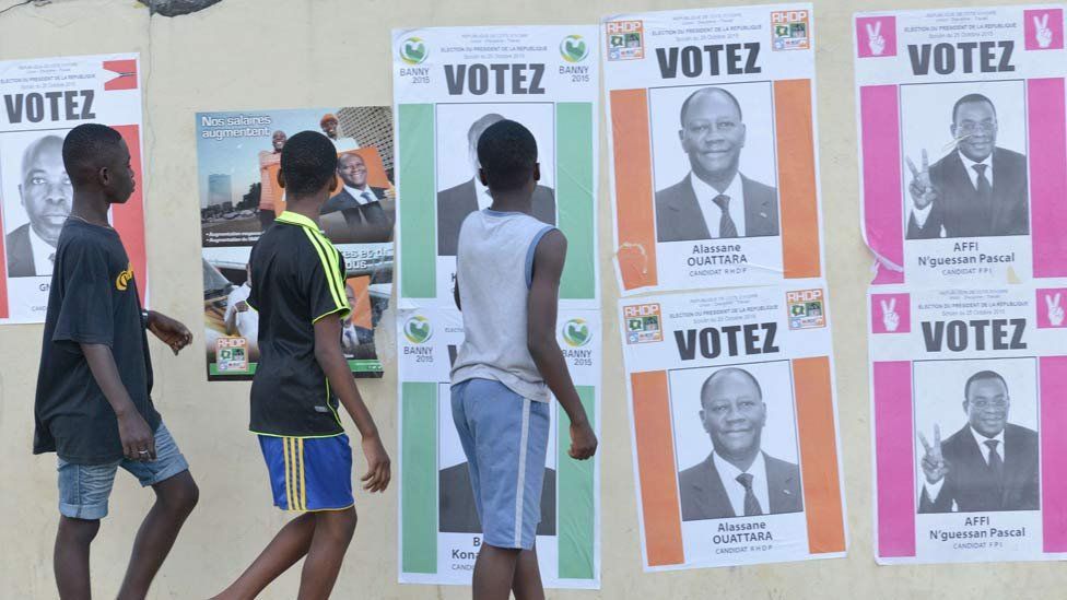 Boys walk past Ivory Coast's presidential election candidate campaign posters on October 14, 2015 in Cocody, Abidjan