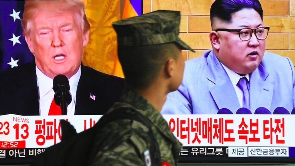 A South Korean soldier walks past a TV screen showing pictures of US President Donald Trump and North Korean leader Kim Jong Un at a railway station in Seoul