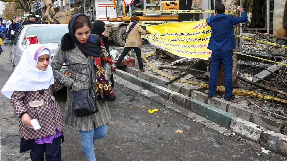 Woman and child walk past debris following anti-government protests in Tehran (20/11/19)