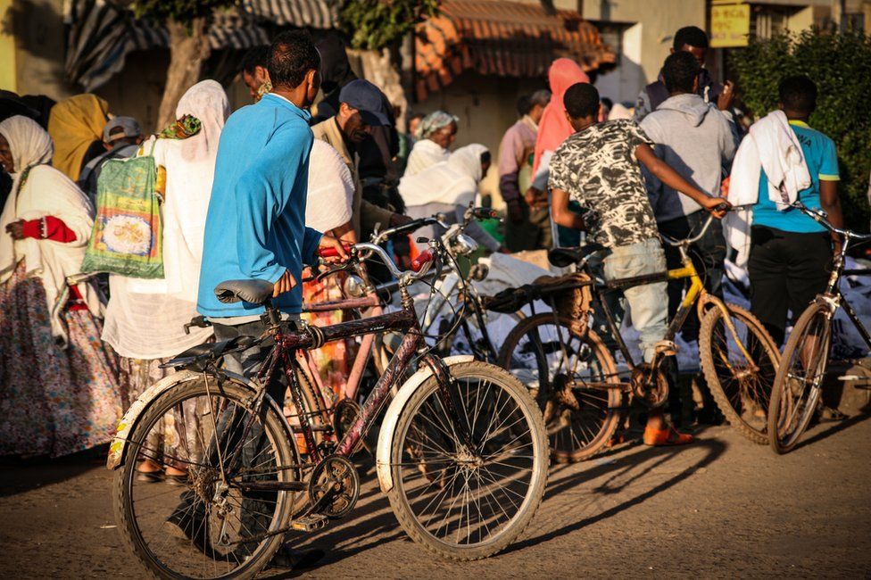 People with bicycles walking past street stalls in Asmara, Eritrea