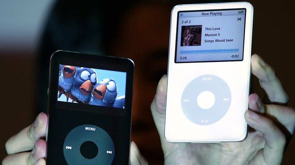 A pair of hands holds up two iPod video models in black and white - one is playing a movie, the other music
