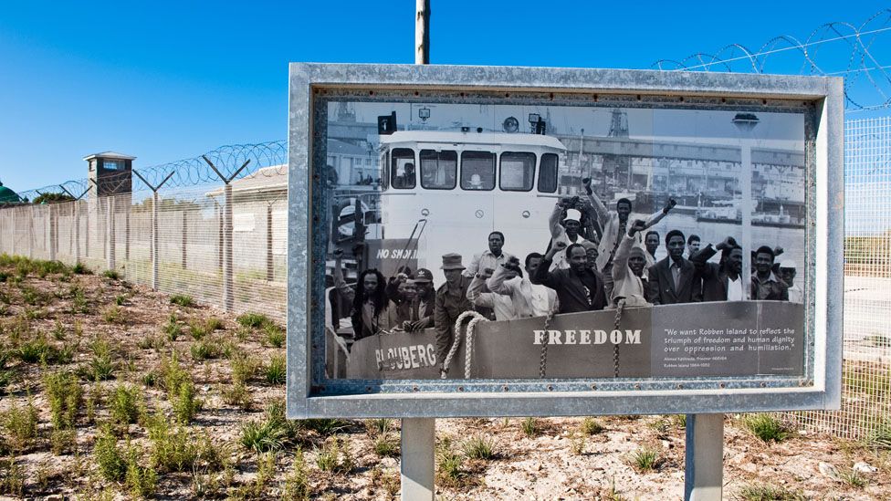 Poster showing prisoners freed from Robben Island, outside the prison itself