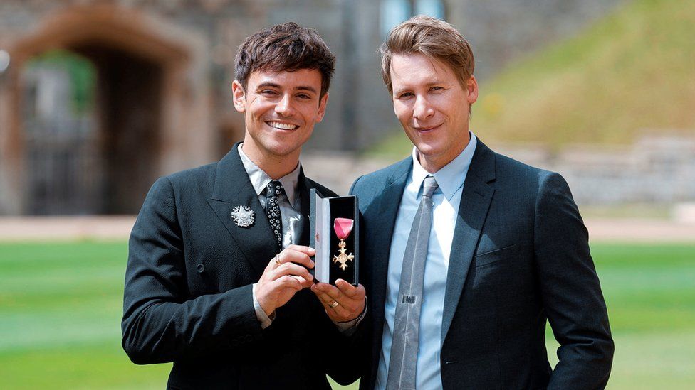 Tom Daley next to his husband Dustin Lance Black with his OBE