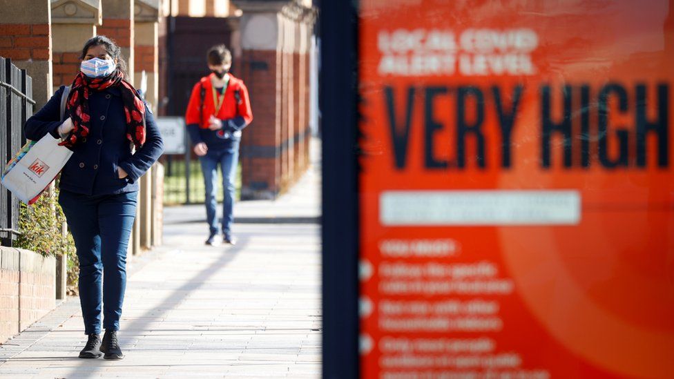 Person in Liverpool walking past a poster saying Covid levels are "very high"