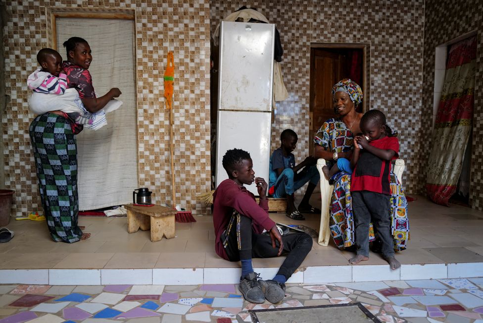 Fallou Diop sits next to his mother Ndeye Boye and brothers and sister, who is carrying her son, at their home in Niaga, Senegal, 28 January 2021