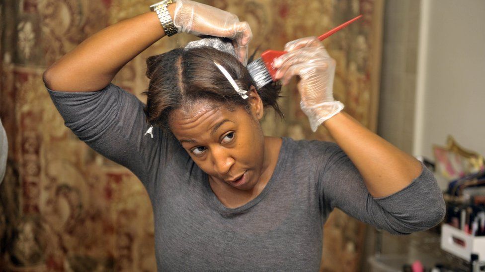 A woman with afro-texture hair puts in hair relaxer to straighten hair