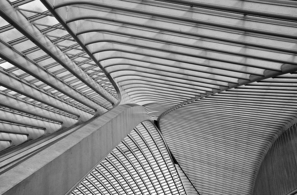 A black and white photo of a train station ceiling made out of metal and glass