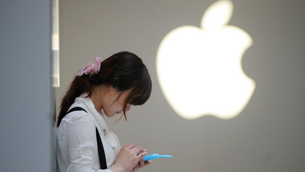 A woman stands in front of an Apple logo in China