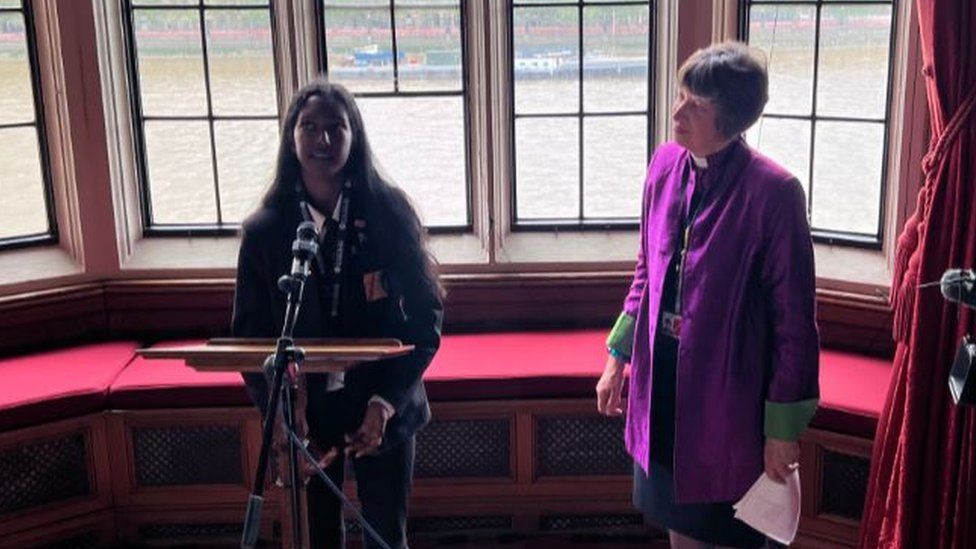 A young black girl speaking into a mic next to a bishop in purple