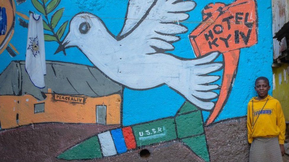 A girl poses by a street mural created by a group of Artists from Maasai Mbili depicting a sign of love from Kibera to Ukraine a midst the war