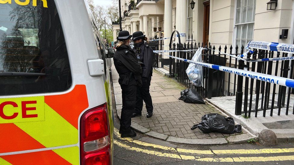 Two police officers standing beside police tape attached to railings around door