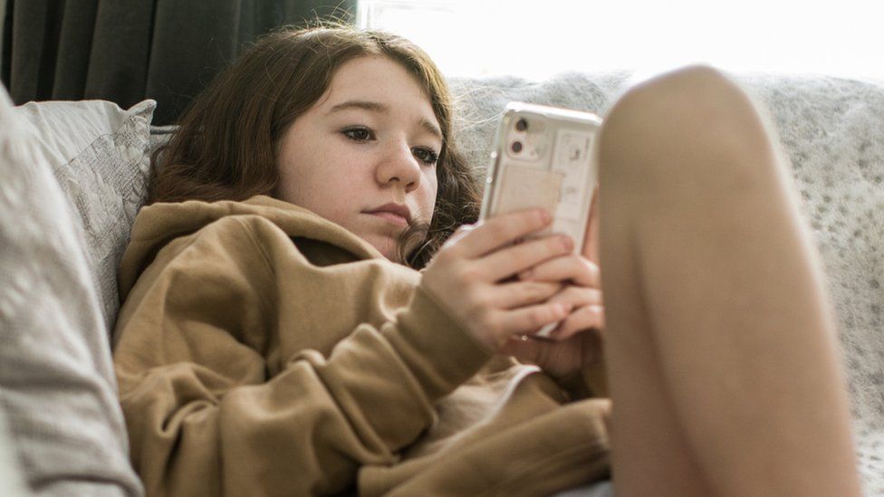 Изображение подростка, сидящего на диван смотрит в свой телефон