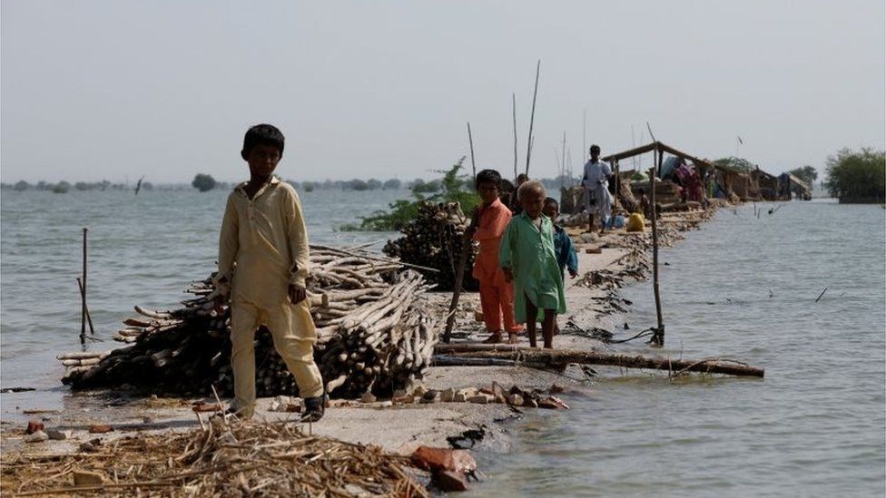 Дети стоят, когда их семья укрывается на поврежденной дороге во время наводнения после дождей и наводнений в сезон дождей в деревне Баджара, на берегу озера Манчар, в Сехване, Пакистан, 6 сентября 2022 года.