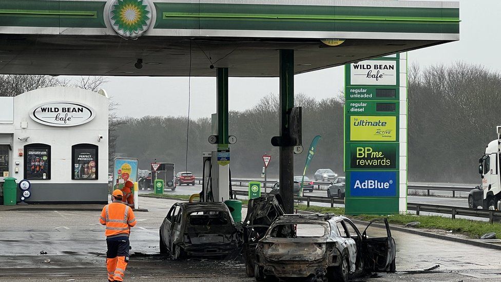 The burnt-out shells of two cars on a petrol forecourt