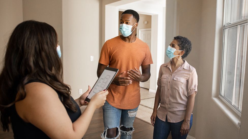Stock image of an estate agent and a couple wearing face masks, on a house viewing