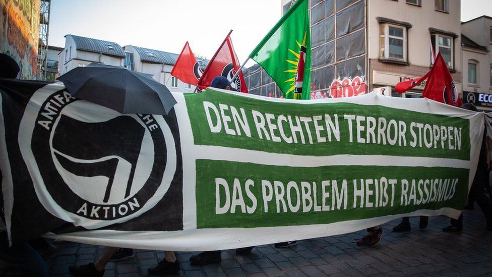 Flags are raised above an anti-fascist demonstration, behind a banner reading, in German, "Stop the far-right terror, the problem is called racism"