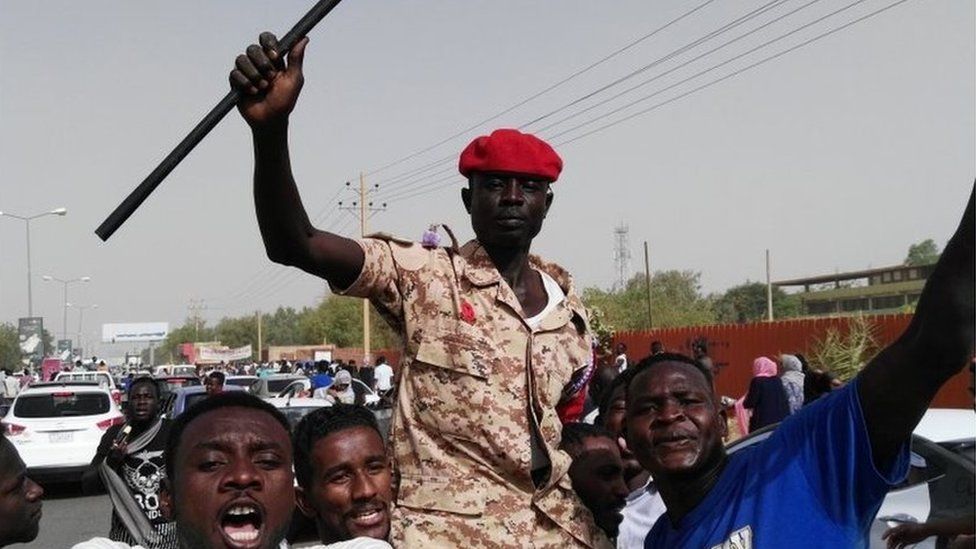 Sudanese men chant slogans as a soldier imitates President Omar al-Bashir waving his trademark cane, on April 11, 2019 during a rally in the capital Khartoum.