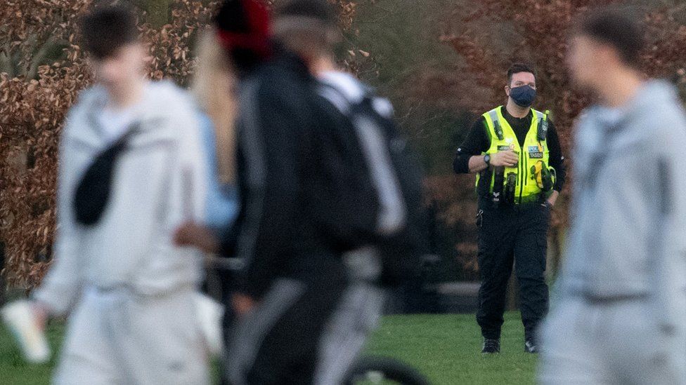 A police officer in a park with a group of unidentifiable men in the foreground