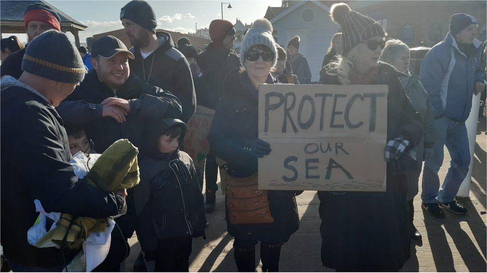 A woman holds a sign saying 'protect our sea'